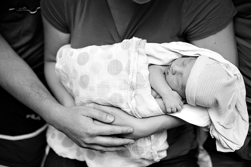 Image from above of a newborn baby surrounded by his parent's arms.