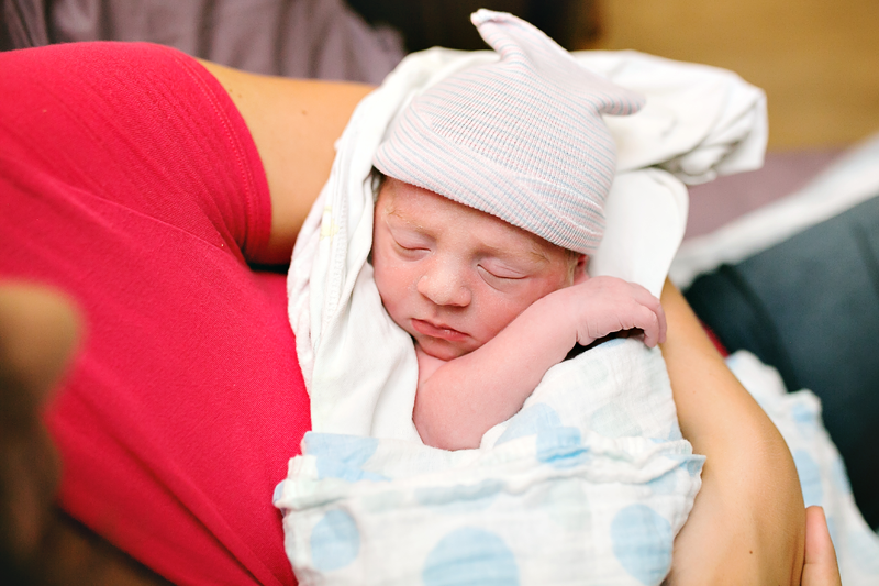 Image of a newborn baby, swaddled in his mama's arms.