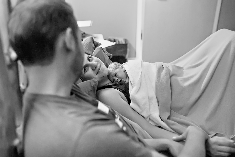 Image of a mother smiling at her partner with her newborn resting on her chest.